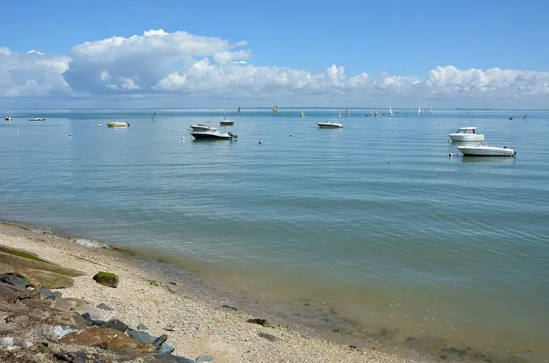 Small boats sit at anchor in calm, pale water off La Flotte on the coast of Ile de Re.