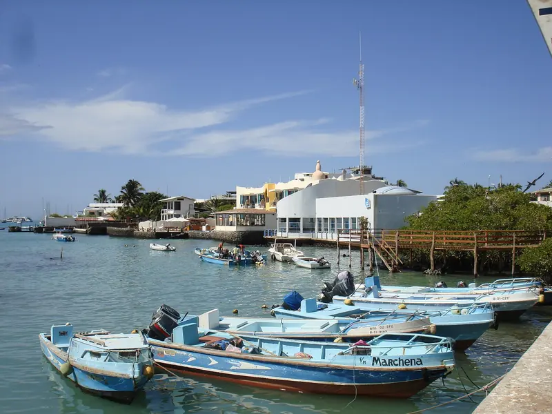Local pangas and skiffs tied up on the Puerto Ayora waterfront, where a visiting yacht clears in with the Capitania and a licensed agent.