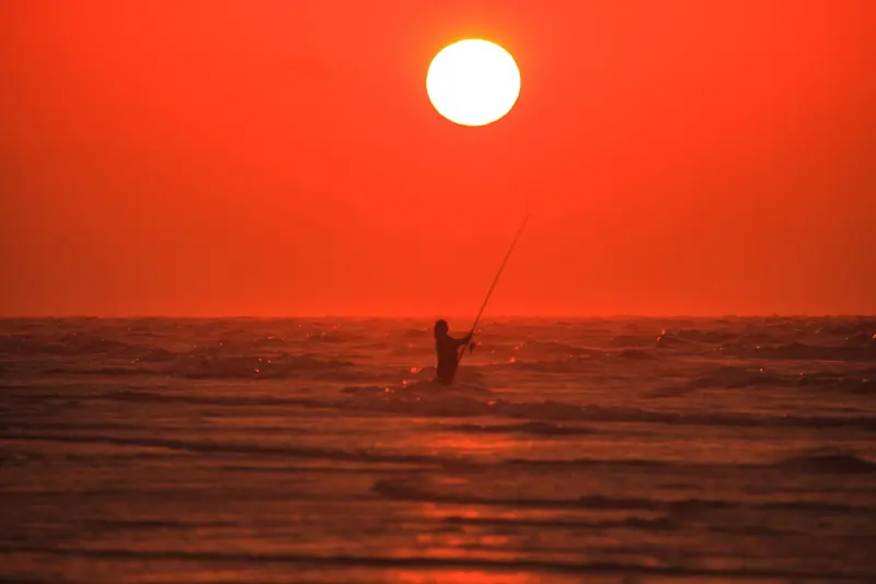 A fisherman silhouetted against a Kimberley coast sunset, on one of the region's famous red-sand beaches.