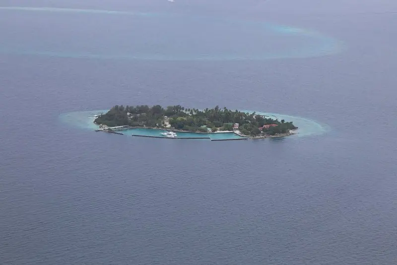 Far out on the atoll rim a single island carries its resort, the reef showing pale around it and the water dropping away dark on every side.