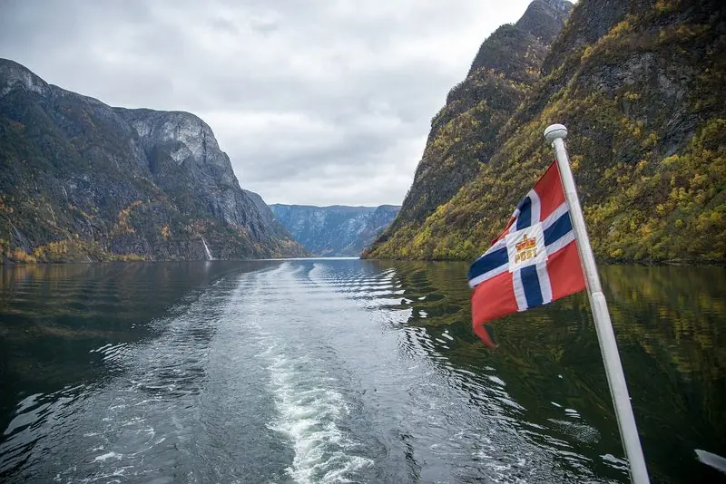 Norway's ensign stands out over the wake as a boat runs the length of the Naeroyfjord, the walls rising sheer on both sides.