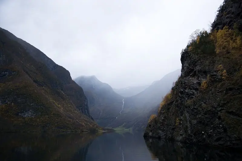 Low cloud sits on the Naeroyfjord in autumn, the water dead flat and a waterfall dropping into the head of the reach.