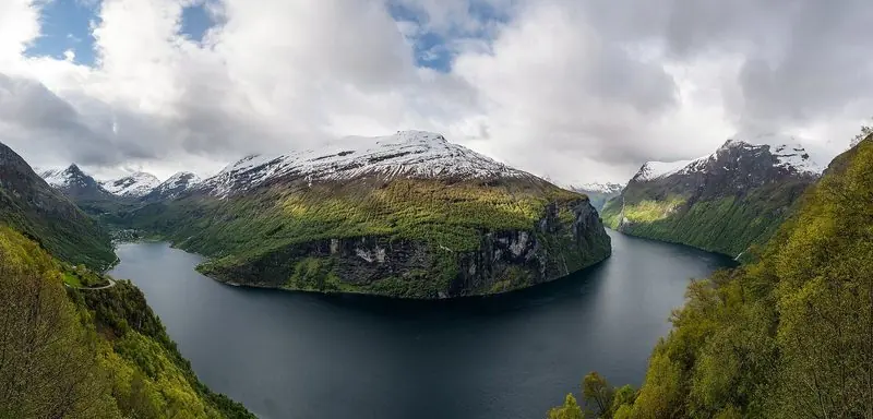 Snow-capped ridges frame the bend in the Geirangerfjord, with the village and its quay just visible at the far end.