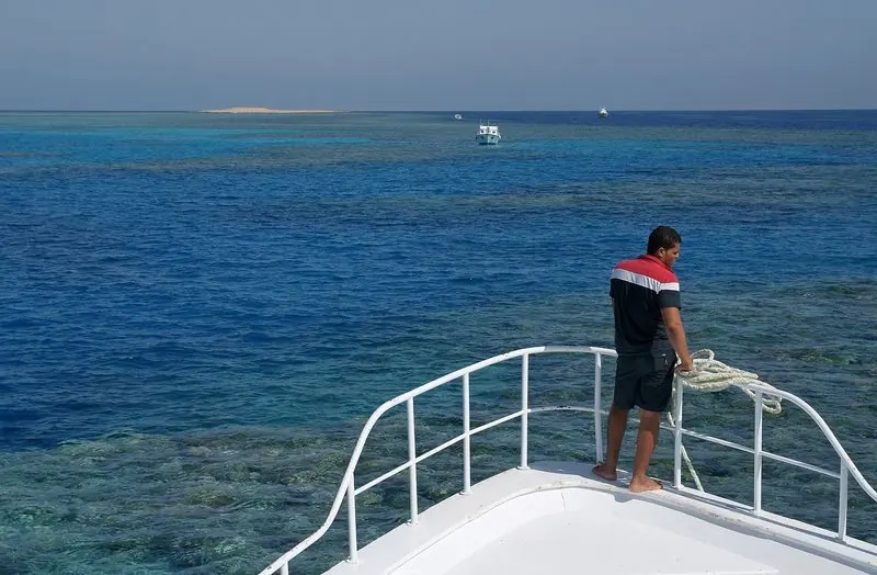 Flat turquoise water and a bare desert ridge frame a classic wooden motor yacht lying moored in the lagoon at El Gouna.