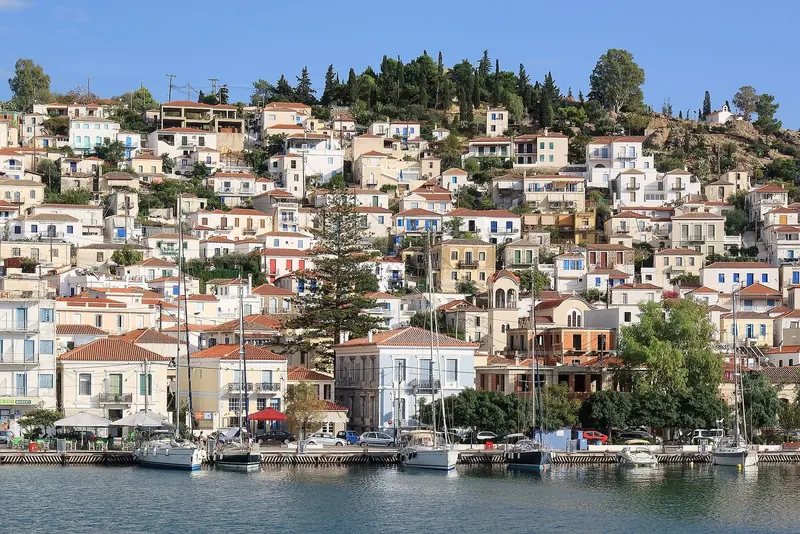 Blue shutters and whitewashed walls line a steep lane in Poros, the close-set island architecture that keeps the alleys shaded at midday.