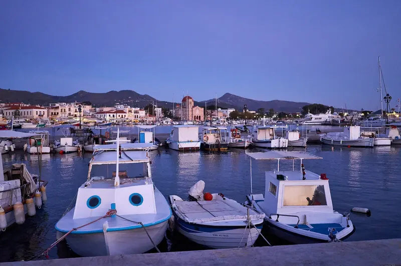 Small fishing boats crowd the quay at Aegina, with the Church of the Presentation of the Virgin Mary standing above the harbour beyond.