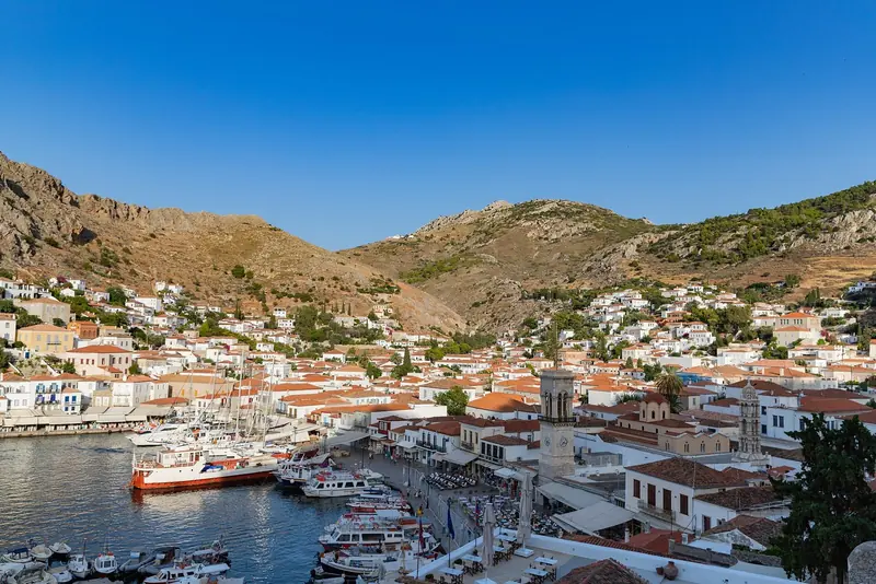 The full sweep of Hydra's waterfront, stone houses and shuttered windows facing directly onto the quay where ferries and water taxis tie up.