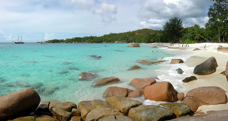 Boulders and pale sand under shallow turquoise water, in a group that sits outside the cyclone belt and never closes for a season.