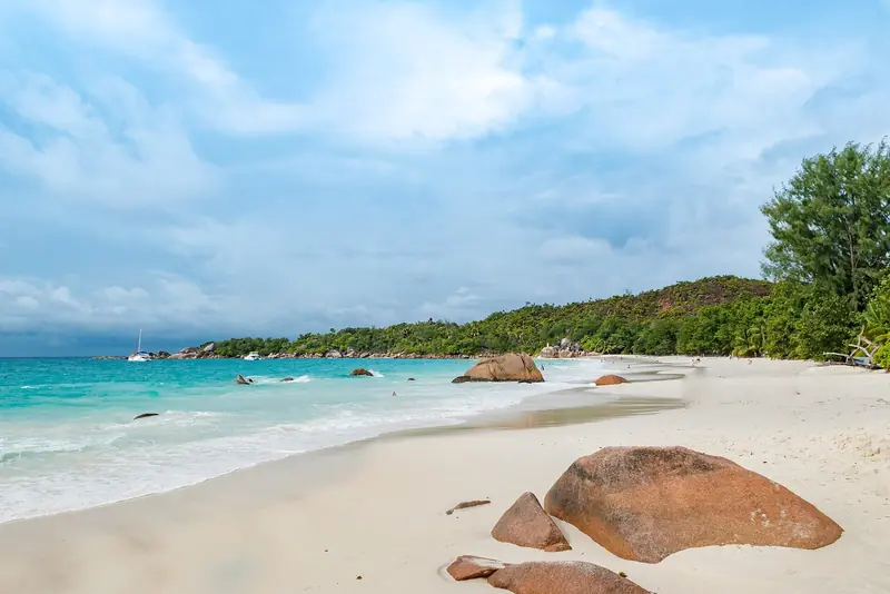 A yacht lies off a beach of sand and boulders, on an island group where anchoring off is often the alternative to the one marina.