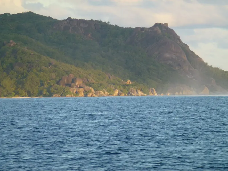 A steep forested island seen from the sea, the inner group rising to 900 metres on Mahe rather than sitting flat like an atoll.