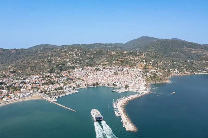 A ferry arriving at Skopelos harbour, the amphitheatre of red-roofed houses behind it.
