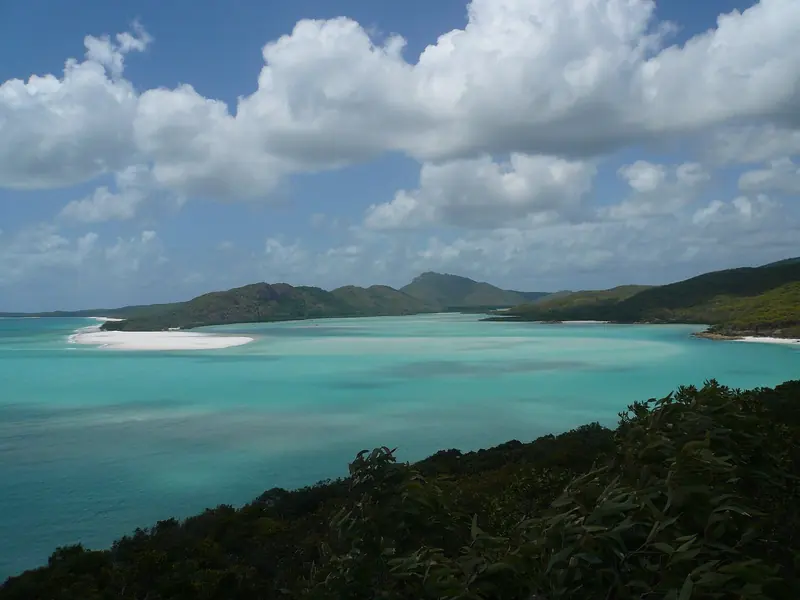 A sand spit and shallow turquoise water between forested islands, which are drowned mountain tops rather than coral cays.