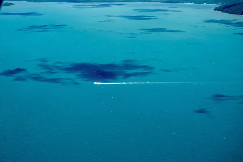 The edge of a reef seen from the air with a boat crossing it, inside a Marine Park zoned with no anchoring areas and public moorings.