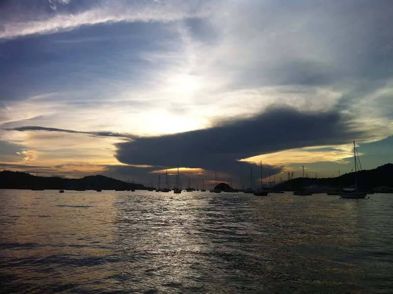Yachts lie at anchor in Chaguaramas Bay at sunset, the masts of the boats that lay up here for hurricane season silhouetted against the evening sky.