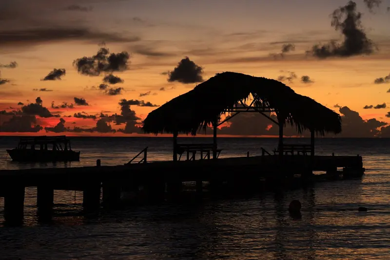 A thatched-roof jetty at Pigeon Point on Tobago's southwest coast, with a tour boat moored alongside at sunset, the island's better-known face as a cruising stop.