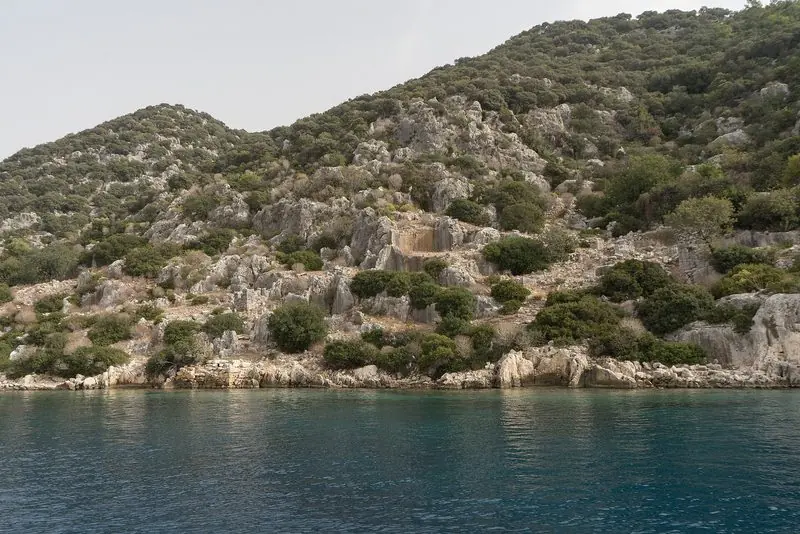 Wild limestone shore drops straight into deep blue on the Turkish coast, courses of ancient wall still visible at the waterline and nowhere along it to land.