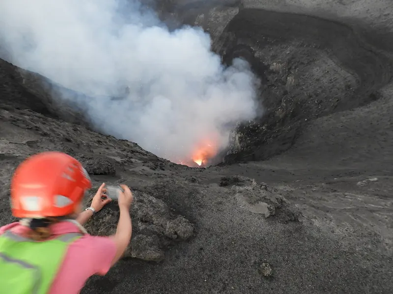 A visitor photographs glowing lava from the crater rim of Mount Yasur, one of the few volcanoes in the world open to this kind of close approach.
