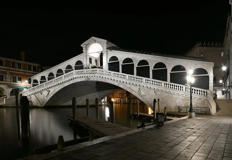The Rialto Bridge at night, lit and empty of the crowds that fill it by day. A superyacht never berths this close; the nearest positions for a large yacht are well outside the historic centre.