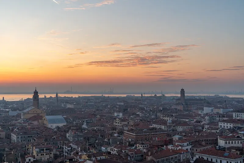 Venice's rooftops toward the lagoon at sunset, the low terracotta skyline that makes the whole city read as one building from the water. The lagoon beyond is where the real navigation problem starts.
