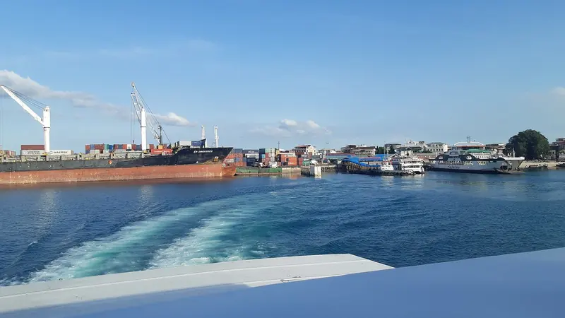A tender's wake crosses Zanzibar's working harbour, container cranes and inter-island ferries sharing the same stretch of water a visiting yacht clears through.