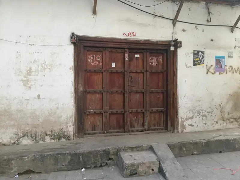 A weathered double door with red Gujarati lettering on a Stone Town street, event posters pinned to the lime-washed wall beside it.