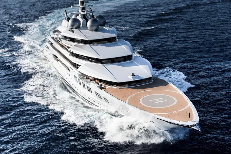 Amadea's bow and helicopter deck seen from above at speed. The forward helipad and the yacht's six-deck profile are part of what a reported 187 million dollar buyer gets for well under a new-build price at this scale.