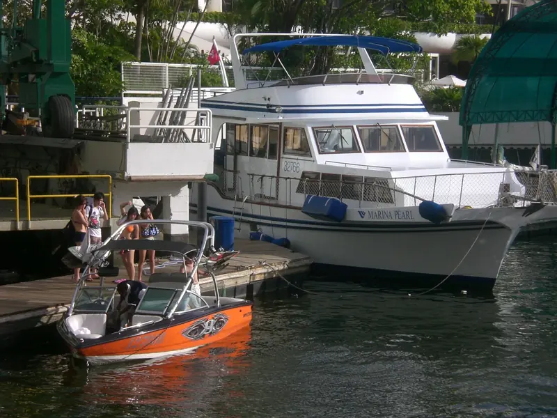 Members boarding an orange wakeboard boat at the Aberdeen Marina Club pontoon, with the motor yacht Marina Pearl berthed behind them.