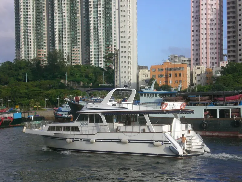 A member's motor yacht underway on the West Typhoon Shelter, Aberdeen's residential towers crowding the shoreline behind it.