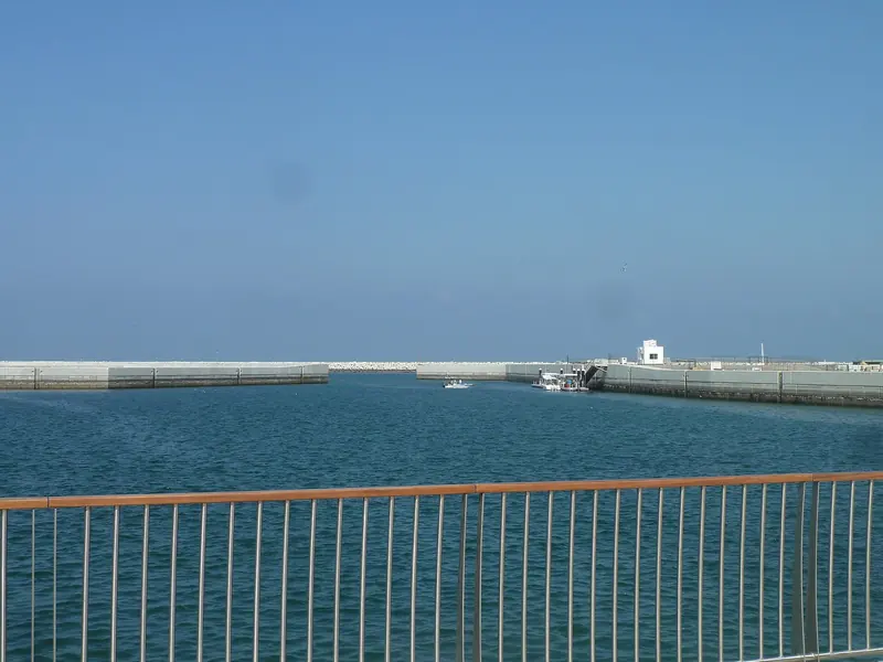 The mouth of the basin from inside. The Gulf of Oman is open water and the swell that runs down it is why the arm is built the way it is.