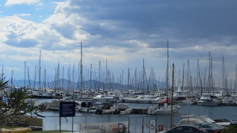 A forest of masts inside the basin, with the Kalamaki Nautical Club's sailing school sign on the fence in the foreground.