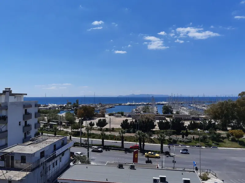 Alimos Marina's basin seen from an apartment balcony above the coast road, moored yachts filling both arms of the harbour.