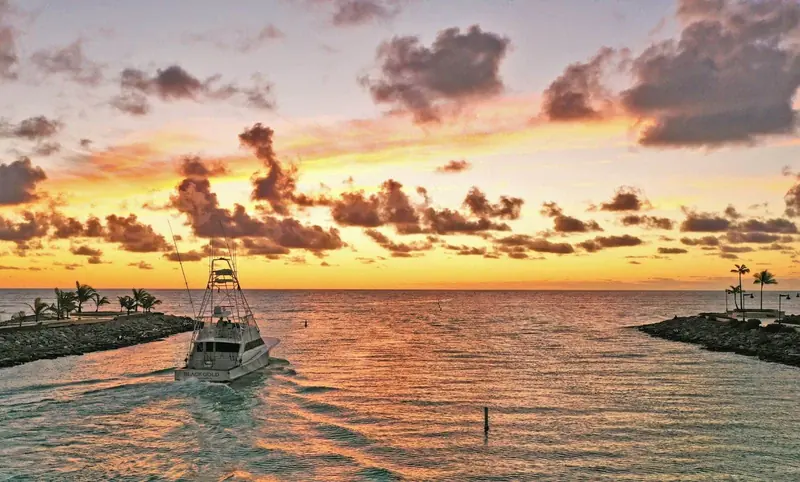 The sportfishing boat Black Gold enters the Cap Cana channel between the breakwater jetties at sunset.