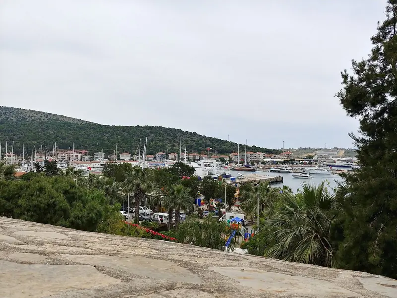 Looking down on the marina and harbor entrance from the castle walls, hills and pine trees framing the bay.