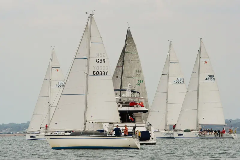 A class of GBR-registered racers close together off Cowes during Cowes Week, crew numbers marked on their hulls.