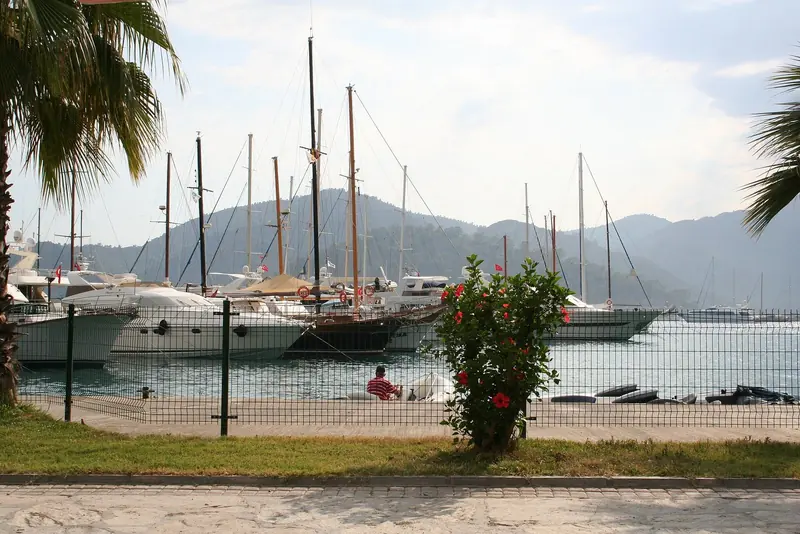 Gulets and motoryachts on the town quay at Gocek, palm trees and Taurus foothills behind.