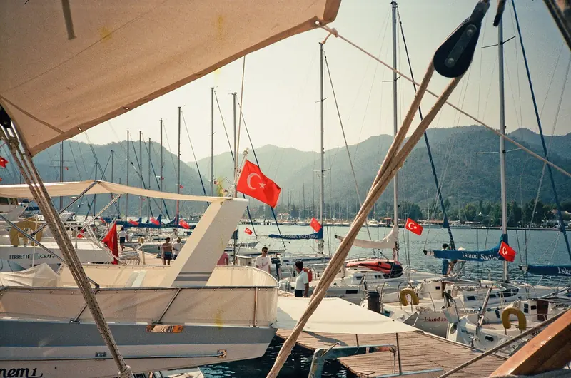 Crewed yachts flying Turkish courtesy flags line the pontoons, Ferretti and Bavaria craft moored gunwale to gunwale.