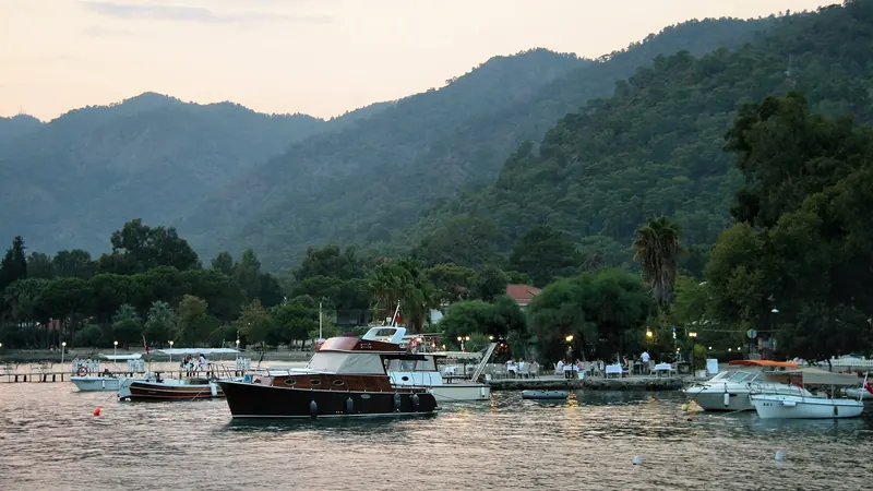 Small craft moored off the promenade at dusk, the wooded hills closing round the anchorage.