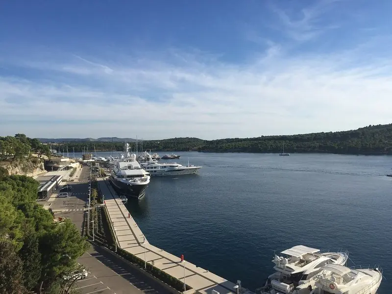 Large motor yachts lie alongside the long outer quay at Mandalina, the basin set into a wooded arm of the Sibenik channel well inside the open sea.