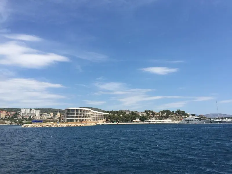 Seen from the water, the marina's outer quay and the curved resort hotel behind it are what you pick up on the way in, with a big white motor yacht already alongside.
