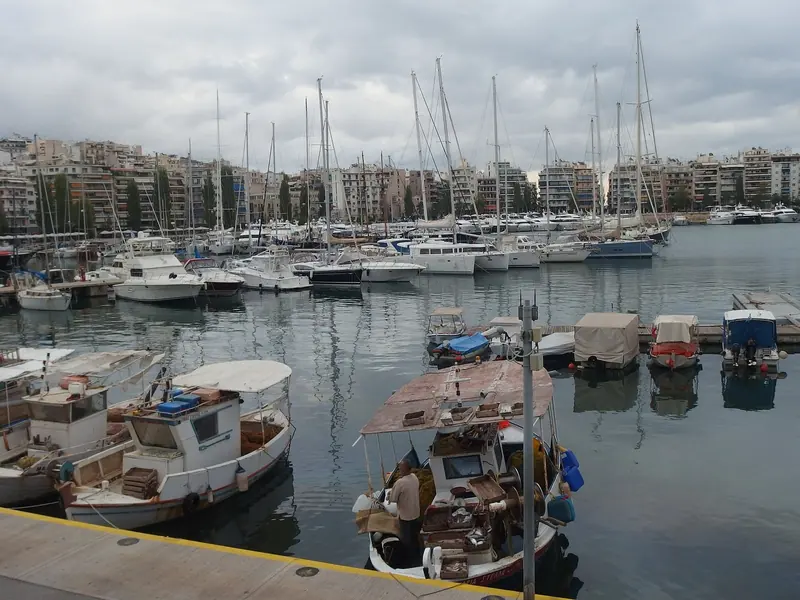 A working fishing caique shares a finger pontoon with sport-fishers and cruisers a few berths away, a reminder that Zea grew up around a Greek harbour rather than being built as a marina from scratch.