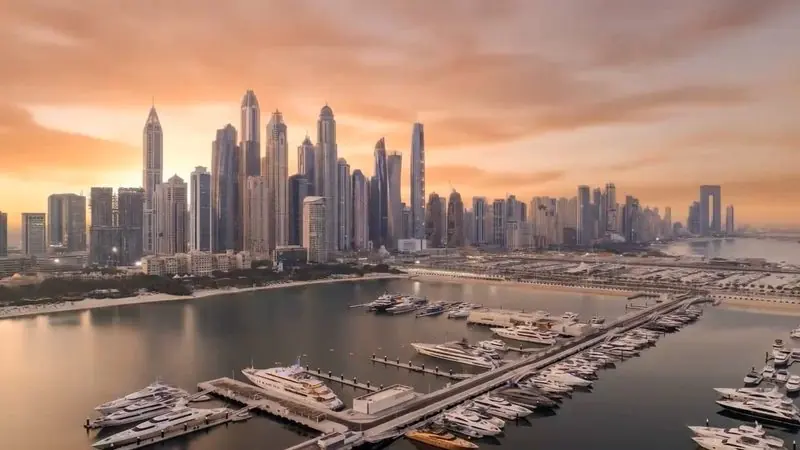 Rows of berthed yachts fill the basin under an orange evening sky and a wall of high rise towers.