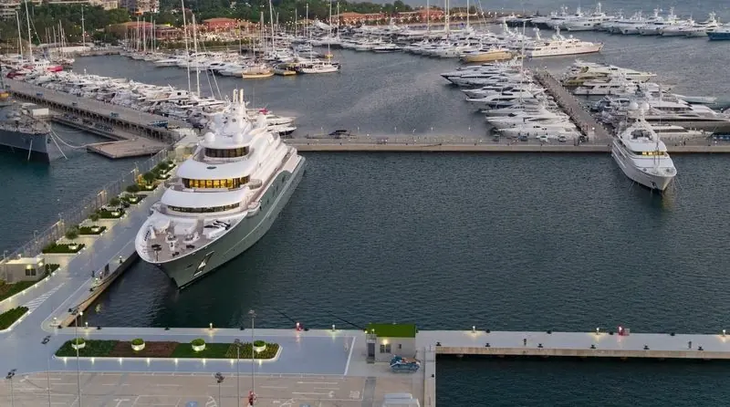 A superyacht alongside the quay, with the promenade and its restaurants a few steps away.