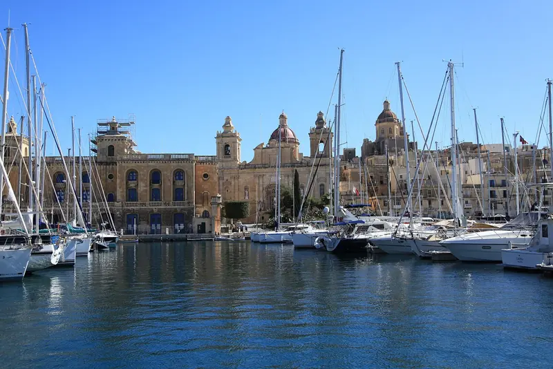 The Birgu quay from a harbour cruise boat. Yachts lie stern-to against the waterfront buildings, which is the whole point of berthing here.
