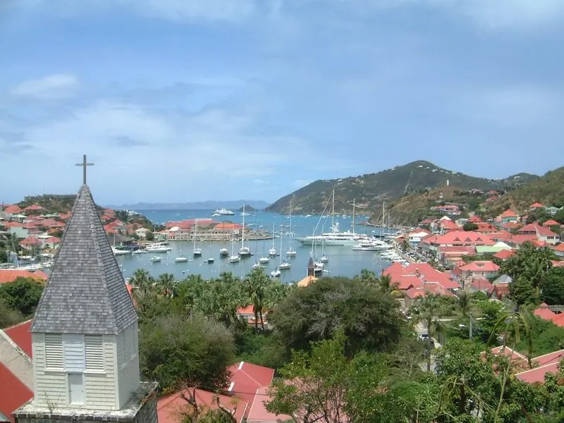 Yachts fill the inner harbour on moorings and along both quays, the town wrapped around the water and the open sea just beyond the entrance.