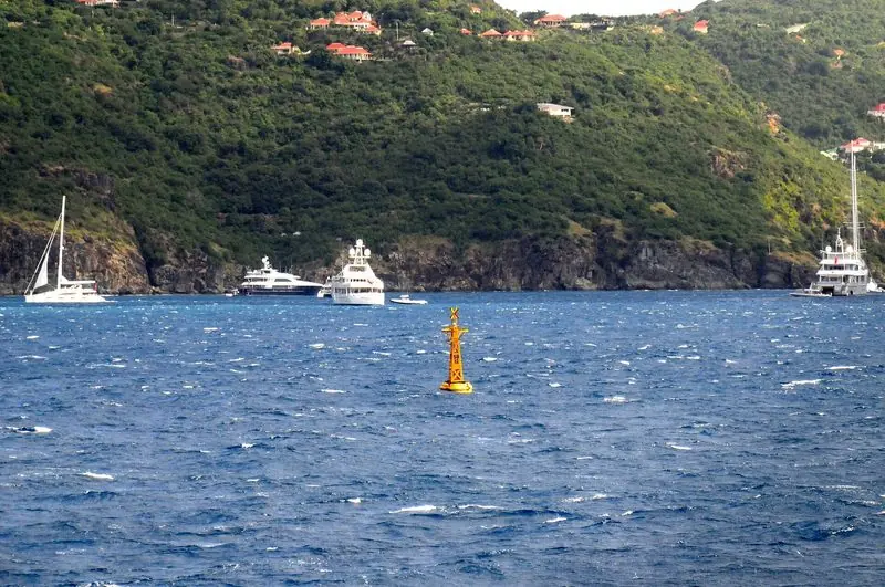 Larger yachts anchor off the entrance in open blue water, the fairway buoy marking the run in to the harbour.