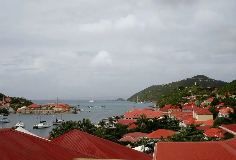 Sailing yachts and catamarans swing to moorings inside the harbour while the deeper anchorage lies out past the headland.