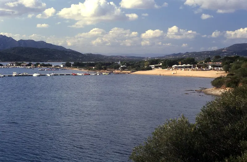 The west shore of the Golfo di Cugnana, small tenders and day boats moored off a beach a short walk from the marina basin - the scale of craft the bay handles outside the megayacht berths.