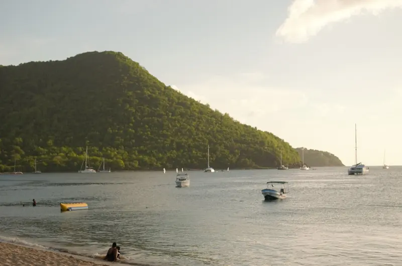 Pigeon Island's headland closes off the north end of the bay; boats ride at anchor in its lee while swimmers use Reduit Beach in the foreground, a five-minute walk from the marina gate.