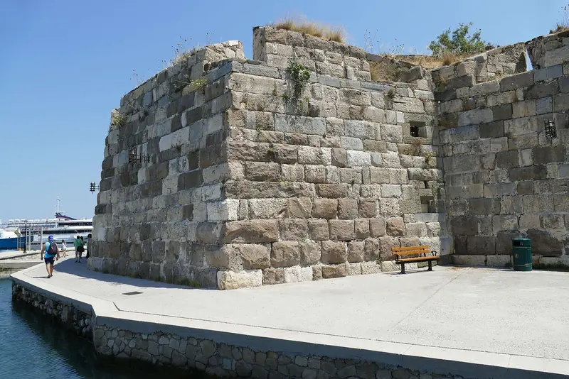 The medieval walls of the Neratzia castle, with yachts moored in the marina visible just beyond.