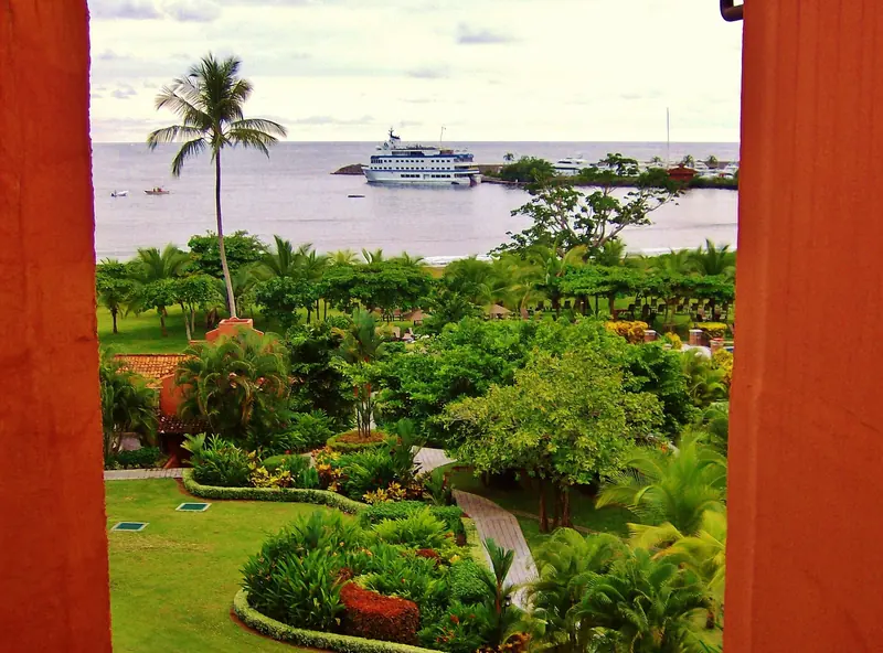 The marina entrance and moored boats at Los Suenos, framed between a resort balcony and the palm-lined lawn running down to Herradura Bay